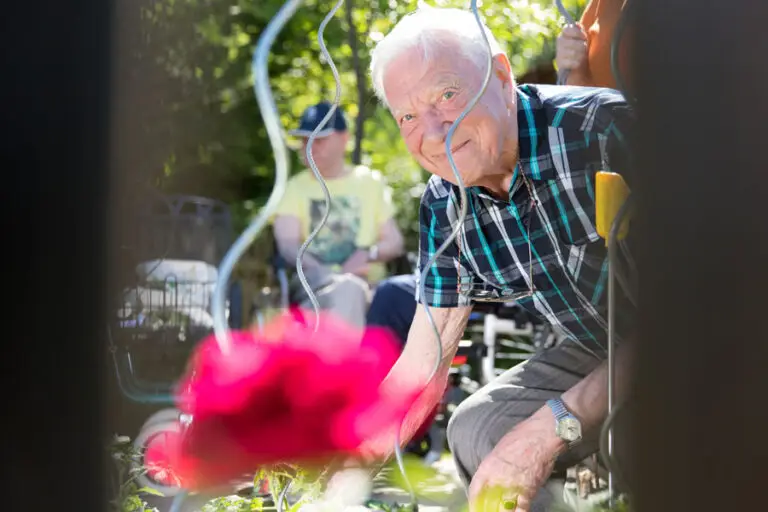 Älterer Mann arbeitet im Garten und blickt lächelnd in die Kamera.