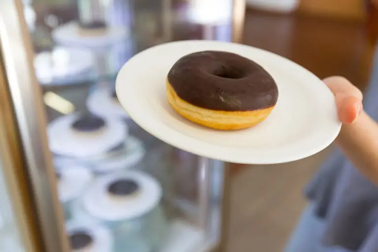 Teller mit Schokoladen-Donut wird vor einer Kuchenvitrine präsentiert.
