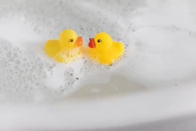 Zwei gelbe Gummienten schwimmen gemeinsam im Schaum eines Pflegebads.